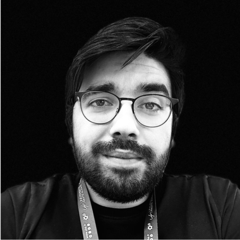 Portrait en noir et blanc de João, lunettes et barbe, fond noir.